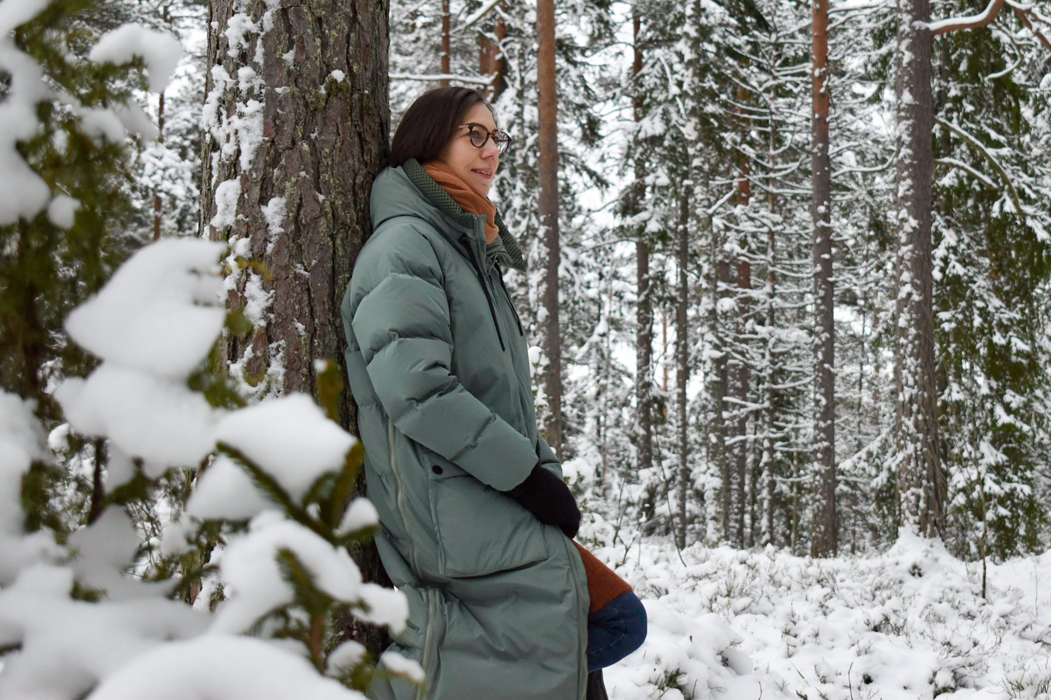Meri Korpilahti, puheterapeutti, nojaa puuhun lumisessa metsässä.