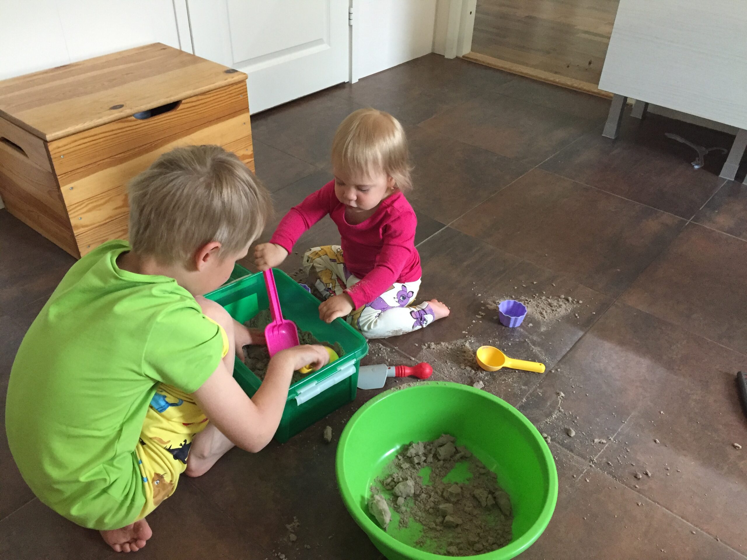 Kaksi lasta leikkii lattialla hiekalla ja lapioilla.